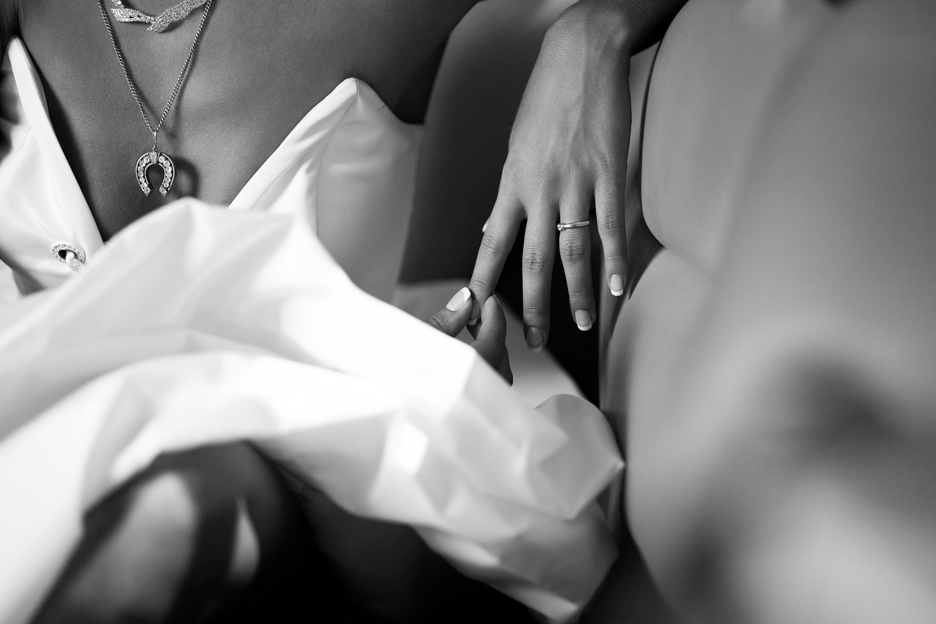 Close-up of a woman's hand with a ring, touching her silk dress; a horseshoe pendant necklace adds depth and emotion.
